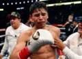 Ryan Garcia is visibly emotional in the ring, flanked by two team members, with one placing a hand on the boxer's chest. The scene is set in a well-lit arena filled with spectators.