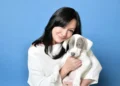 Shannen Doherty, Star of '90210' and 'Charmed,' Dies at 53 After Battle with Cancer with long black hair, wearing a white outfit, holds a white and gray puppy against a blue background.