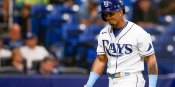 Wander Franco in a Tampa Bay Rays uniform stands on the field. He is holding a bat and wearing a helmet, reminiscent of Wander Franco's stance during crucial moments.