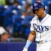 Wander Franco in a Tampa Bay Rays uniform stands on the field. He is holding a bat and wearing a helmet, reminiscent of Wander Franco's stance during crucial moments.