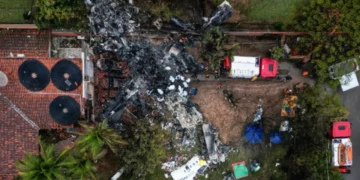 Aerial view of the Vinhedo crash site featuring debris, emergency vehicles, rescue tents, and personnel amidst trees and a building, as covered in aviation accident news.
