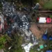Aerial view of the Vinhedo crash site featuring debris, emergency vehicles, rescue tents, and personnel amidst trees and a building, as covered in aviation accident news.