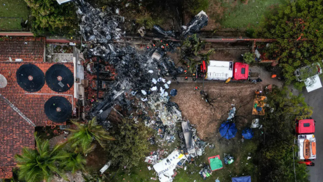 Aerial view of the Vinhedo crash site featuring debris, emergency vehicles, rescue tents, and personnel amidst trees and a building, as covered in aviation accident news.