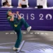 Rachael 'Raygun- Gunn in a green uniform performs a kick during a taekwondo event at the Paris 2024 Olympics, with judges seated at a table in the background.