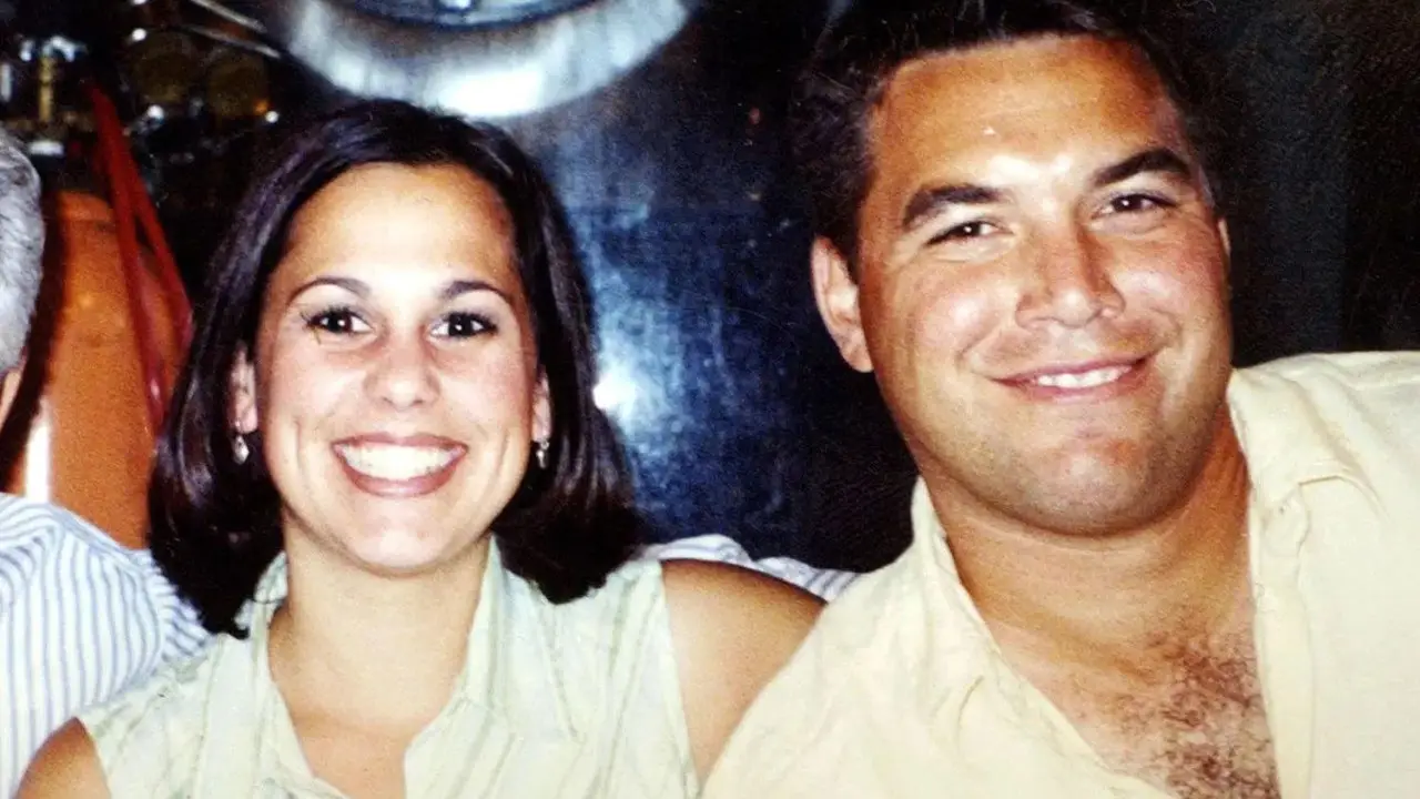 A man and woman smile at the camera while sitting closely together, their expressions masking a tragic past linked to the notorious 2002 murder involving Scott Peterson’s wife and unborn child. The background is slightly blurred.