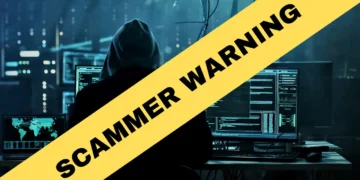 A person in a dark room sits at a computer with multiple screens displaying data. Overlaid in yellow text reads "SCAMMER WARNING," as the Kenosha sheriff warns of scammers targeting residents.