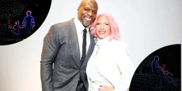 A man in a grey suit and a woman with pink hair in a white outfit stand closely together, both smiling at the camera. The background has circular inserts showing light designs of people. You might even mistake them for Terry Crews and his wife Rebecca sharing a joyful moment.