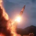Amidst silhouetted hills, a rocket launches into the evening sky, bright flames and smoke marking its ascent—a scene reminiscent of North Korea's missile testing that often stirs global tensions.