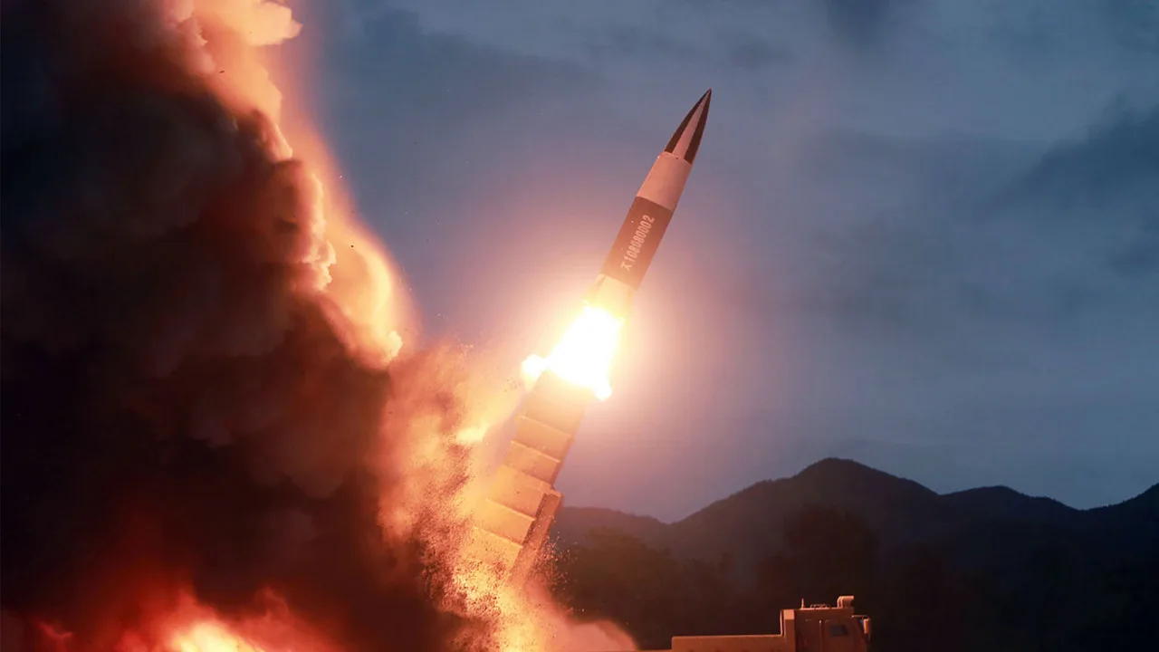 Amidst silhouetted hills, a rocket launches into the evening sky, bright flames and smoke marking its ascent—a scene reminiscent of North Korea's missile testing that often stirs global tensions.
