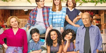 A group of eight people pose in front of a garage, including four seated and four standing. They are smiling and wearing casual clothing, reminiscent of a scene from Netflix multi-cam comedies. The setting includes garage items in the background, capturing an everyday moment worthy of Kurtwood Smith's Instagram.