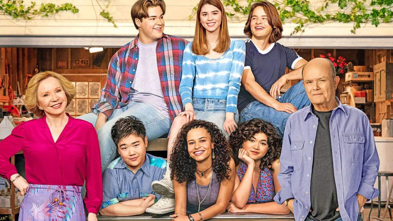 A group of eight people pose in front of a garage, including four seated and four standing. They are smiling and wearing casual clothing, reminiscent of a scene from Netflix multi-cam comedies. The setting includes garage items in the background, capturing an everyday moment worthy of Kurtwood Smith's Instagram.