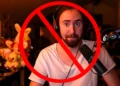 Amidst a backdrop of gaming gear, a figure with headphones and a microphone is crossed out by a red prohibition symbol, signaling Twitch's strict stance on hate speech policy enforcement.