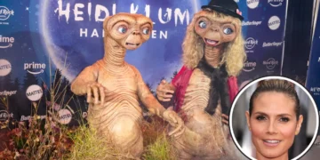 Two people dressed as E.T. characters at a costume event with a themed backdrop capture the spirit of Halloween costumes. Inset shows Heidi Klum's face, adding an extra touch of celebrity charm to the scene.