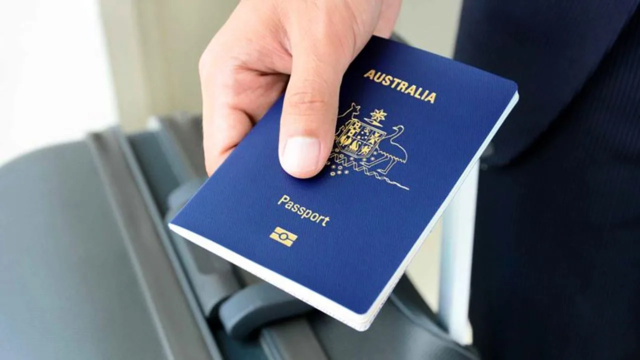 A person holds an Australian passport above a suitcase handle, ready for their journey before the passport fees rise in January.