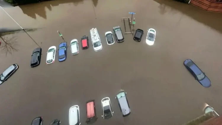 Aerial view of multiple cars partially submerged in floodwater in a parking lot, a result of the torrential rain sweeping through North-West England.